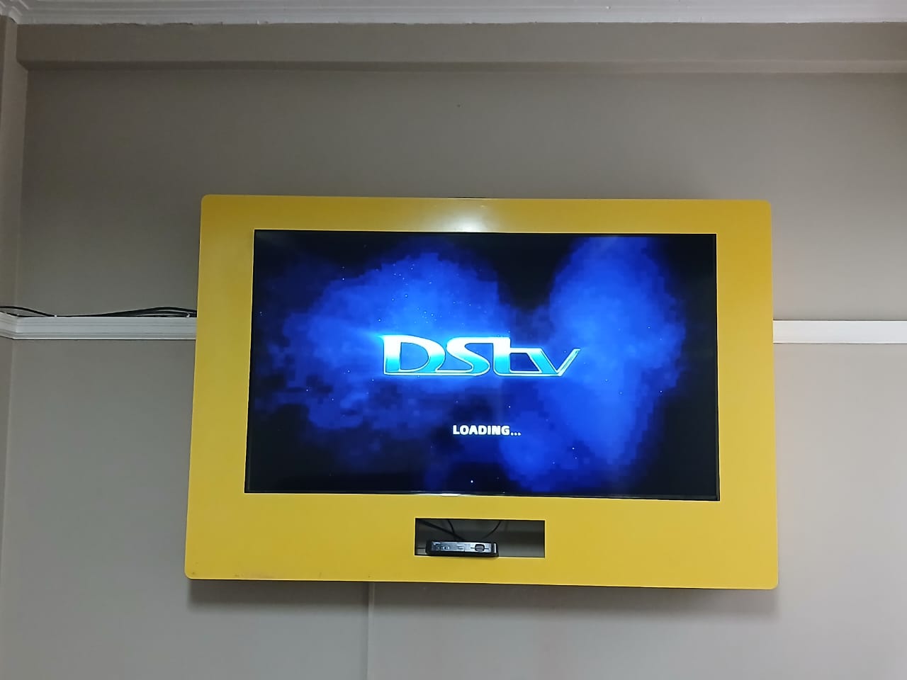 Wall-mounted TV showing the DStv loading screen after installation